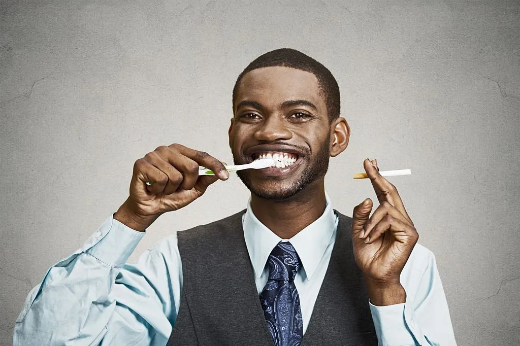 Man brushing his teeth while holding cigarette